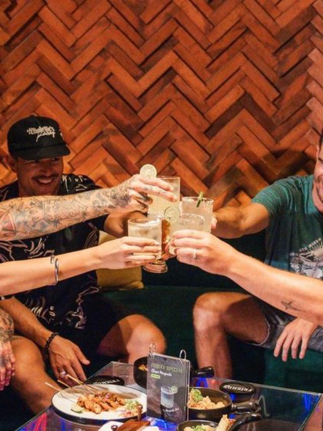 Friends toasting cocktails in a warm brick-lined bar