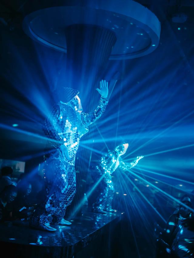 Performers in mirrored suits lit by blue lasers on a nightclub stage