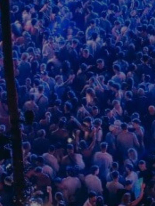 A festival-scale crowd under blue light between palm trunks