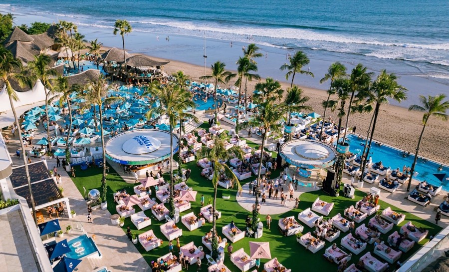 Aerial view of a beachfront pool club with daybeds and swim-up bar